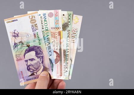 Denaro colombiano - Pesos in mano su sfondo grigio Foto Stock