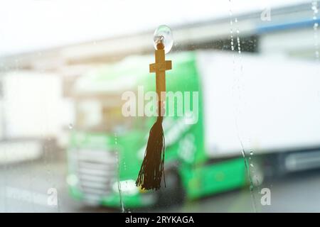 Sul parabrezza nella cabina del camion è appesa una croce - la crocifissione di Gesù. C'è un carrello verde sullo sfondo sfocato. Foto Stock