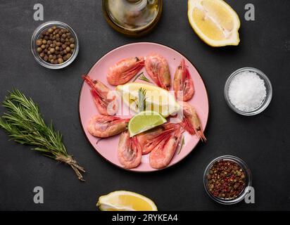 Gamberi bolliti, fettine di limone e lime, spezie su un tavolo nero, vista dall'alto Foto Stock