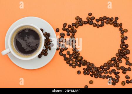 Tazza di caffè su un piattino con chicchi di caffè piegati a forma di cuore Foto Stock