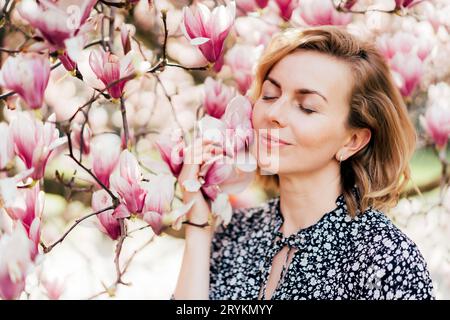Ritratto di una bella donna negli anni '40. Profilo ritratto con un albero di magnolia fiorito rosa come sfondo. Foto Stock