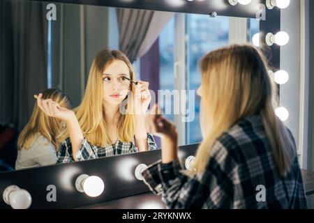 Elegante ragazza indossa il mascara sulle ciglia. La ragazza nel camerino di fronte allo specchio fa un trucco. persona prima di t Foto Stock