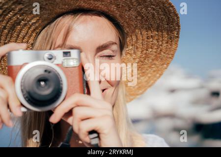 Ritratto ravvicinato di una fotografa viaggiatrice con un cappello di paglia che scatta foto con la fotocamera nelle soleggiate giornate estive. Il professionista prende Foto Stock