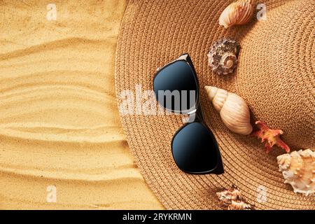 Concetto di vacanza estiva. Cappello di paglia, occhiali da sole e conchiglie sulla spiaggia di sabbia con spazio per copiare i testi Foto Stock