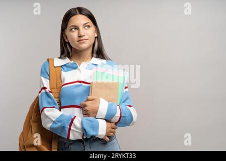 Interessata studentessa seria adolescente con zaino, copia libri su sfondo grigio. Foto Stock