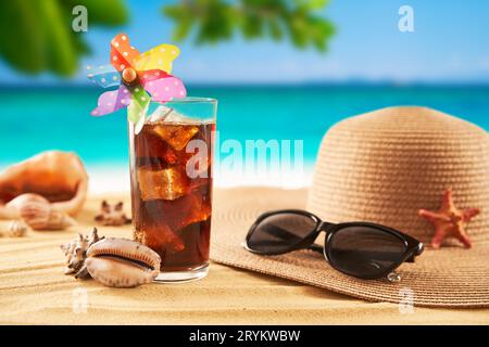 Cappello di paglia, occhiali da sole e cocktail sulla sabbia e sullo sfondo del mare. Rilassati sulla spiaggia Foto Stock