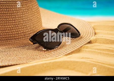 Concetto di vacanza estiva. Cappello di paglia, conchiglie sulla spiaggia di sabbia e sullo sfondo del mare Foto Stock