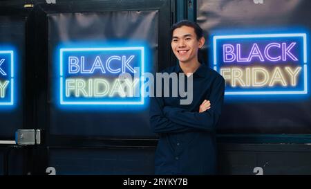 Cliente di un negozio di abbigliamento il Black friday che offre offerte speciali e grandi promozioni, alla ricerca di abiti a metà prezzo. Acquirente asiatico che entra nella boutique outlet con striscioni di sconto. Foto Stock