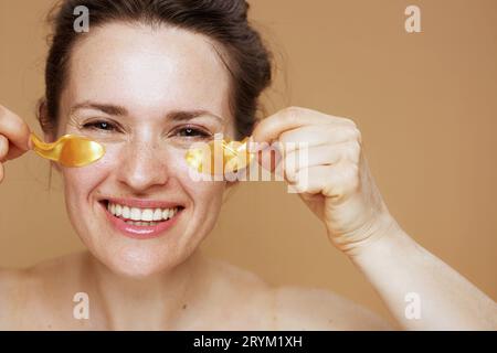 giovane donna sorridente con cerotti oculari su sfondo beige. Foto Stock