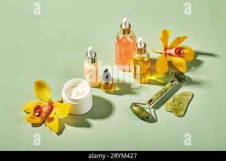 Prodotti cosmetici in bottiglie di vetro con fiori di orchidea - sieri, crema, gel, oli. Concetto per la cura del viso e del corpo, benessere Foto Stock