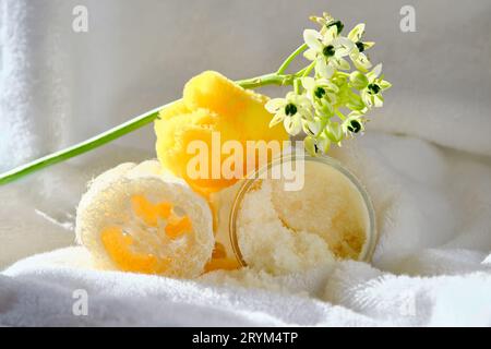 Scrub, salvietta di loofah e spugna marina biologica sullo sfondo di un asciugamano in spugna con fiori. Foto Stock