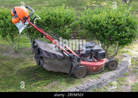 Rasaerba e casco di sicurezza con visiera protettiva e cuffie in giardino Foto Stock