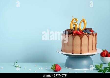 Torta di compleanno al cioccolato con frutti di bosco, biscotti e numero sessanta candele dorate su sfondo blu parete, spazio copia Foto Stock