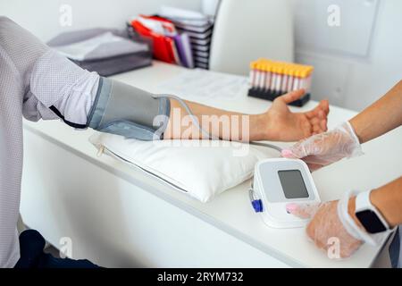 Infermiera in uniforme medica e guanti trasparenti che controllano la pressione sanguigna del giovane in abiti casual. Bruna donna preme B. Foto Stock