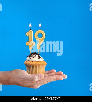 Dolce di compleanno consegnato a mano - candela numero 19 su sfondo blu Foto Stock