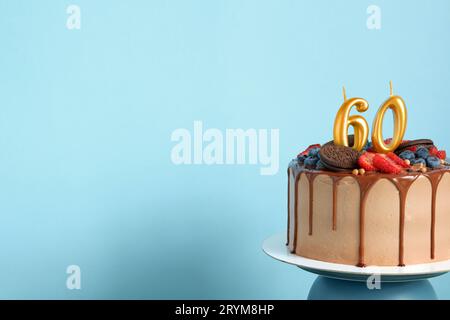 Torta di compleanno al cioccolato con frutti di bosco, biscotti e numero sessanta candele dorate su sfondo blu parete, spazio copia Foto Stock