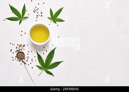 Olio di canapa nel recipiente, foglie e semi su sfondo bianco, stendere in piano con spazio per la copia Foto Stock