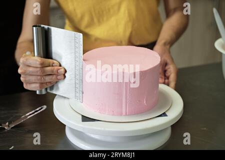 La donna diffonde crema rosa sulla torta, primo piano. Processo di preparazione della torta, messa a fuoco selettiva Foto Stock