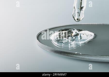 Pipetta con campione di gel di prodotto cosmetico in capsula di Petri su sfondo grigio, ombre dure, messa a fuoco selettiva Foto Stock