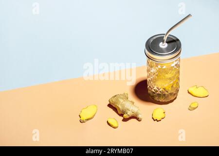 Acqua di zenzero in elegante vaso con cannuccia metallica su sfondo geometrico di carta e fette di zenzero, vista isometrica Foto Stock