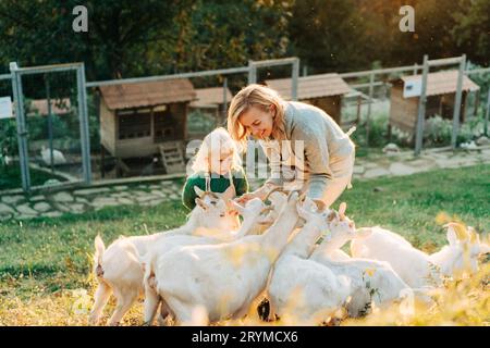 Mamma e bambina nutrono e si preoccupano delle capre nella fattoria. Foto Stock