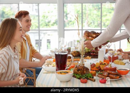 Un giovane che porta il tacchino gustoso a tavola con i suoi amici a casa il giorno del Ringraziamento Foto Stock