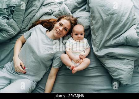 Vista dall'alto di una mamma che si prende cura con un bambino sul letto della camera da letto. Foto Stock