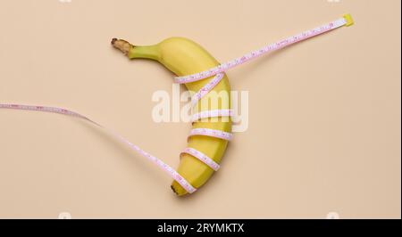 Banana matura gialla avvolta in un nastro di misurazione, concetto di perdita di peso, vista dall'alto Foto Stock