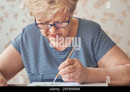 Attraente vecchia donna che dipinge per numeri a casa. Hobby e arte terapeutica ispirati. Messa a fuoco selettiva Foto Stock