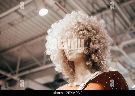 Il manichino in parrucche ricci sta nel negozio di abbigliamento. Shopping, moda e sfondo pubblicitario Foto Stock