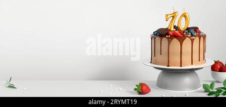 Striscione con torta di compleanno al cioccolato con frutti di bosco, biscotti e numero settanta candele dorate su sfondo bianco, spazio copia Foto Stock