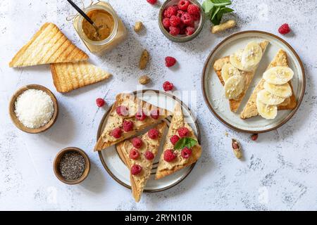 Colazione con sandwich dolci. Gustoso tostato con burro di arachidi, banana e lampone su un tavolo in pietra grigia. fla vista dall'alto Foto Stock