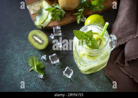 Bevanda rinfrescante estiva con kiwi, cetriolo, lime e ghiaccio, mojito o soda con cetriolo su un tavolo di pietra scura. Foto Stock