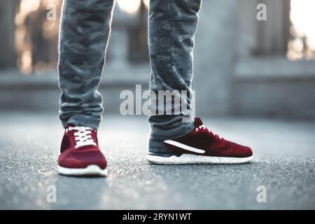 Rosso sport sneakers close-up su asfalto. Gambe e scarpe dal Angolo inferiore Foto Stock