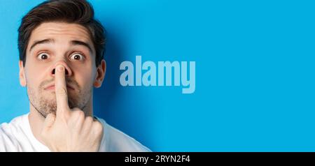 Headshot di un ragazzo caucasico che fa espressioni divertenti, in piedi su sfondo blu Foto Stock