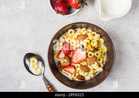 Recipiente con anelli di cereali cheerios, fragole e latte. Colazione tradizionale Foto Stock