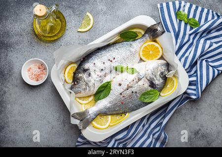 dorado di pesce crudo in casseruola con ingredienti limone, basilico fresco, bottiglia di olio d'oliva su tagliere di legno con coltello Foto Stock