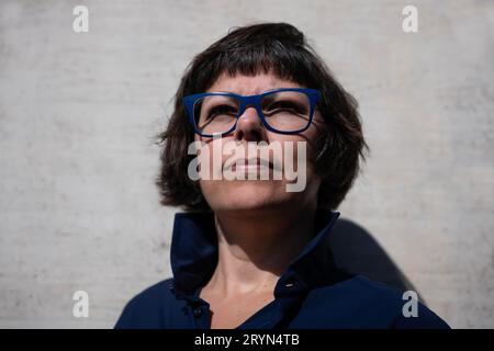 Colpo alla testa su una donna elegante con occhiali da vista e appoggiarsi su un muro di cemento in una giornata di sole in Svizzera Foto Stock