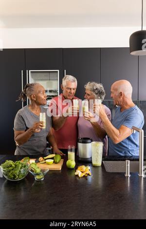 Felice diversi amici anziani che parlano e preparano frullati sani insieme in cucina Foto Stock