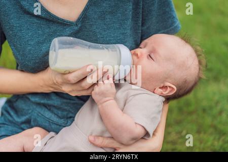 La madre tiene in mano e allatta il bambino dal biberon nel parco. Ritratto di un neonato carino che viene nutrito dalla madre con il biberon. Una donna amorevole che dà Foto Stock