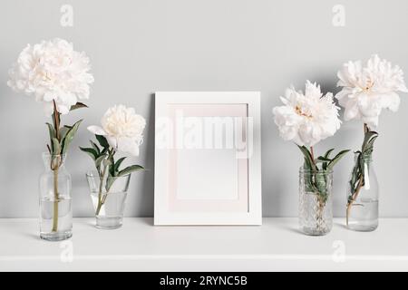 Eleganti fiori di peonie bianche e cornice bianca sullo sfondo della parete del tavolo. Mockup per testo o grafica Foto Stock