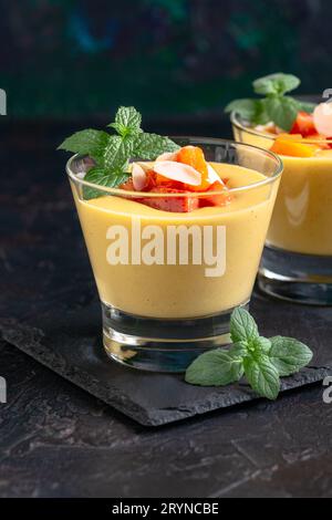 Dessert fatto in casa con latte, panna e pesche fresche in bicchieri servito con fette di menta e pesca fresche, messa a fuoco selettiva. Concetto di dessert cremoso alla frutta Foto Stock