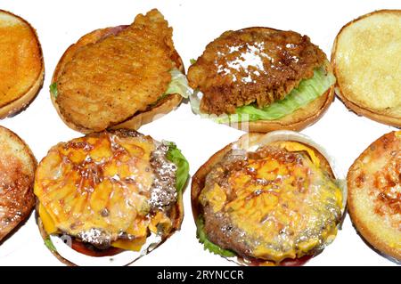 Pila di panini di sesamo di polpettine di filetto di pollo fritto, lattuga croccante, pomodori, formaggio fuso, cipolle e salsa, succosa e spessa polpa di manzo Foto Stock