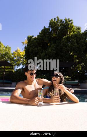 Giovane coppia biraciale che ha limonata e ridere in piedi in piscina, copia spazio Foto Stock