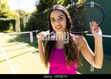 Ritratto di sorridente biraciale bella donna con racchetta da tennis e in piedi in campo da tennis Foto Stock