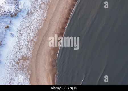 Inverno nella fredda spiaggia innevata del Mar Baltico a Danzica. Vista aerea della spiaggia innevata e delle dune e del paesaggio naturale scuro e calmo Foto Stock