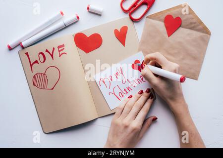 Donna che tiene la penna di feltro-punta e dipinge il biglietto romantico di San Valentino con colore rosso. Foto Stock