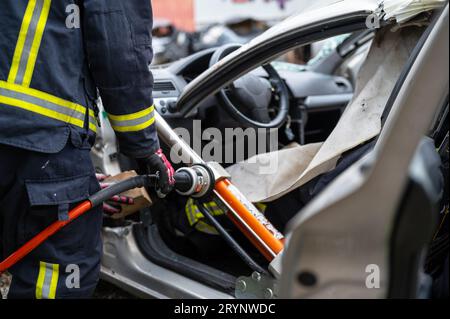 Vigili del fuoco che utilizzano attrezzi idraulici durante un addestramento alle operazioni di soccorso. I soccorritori sbloccano il passeggero in auto dopo un incidente. Foto Stock