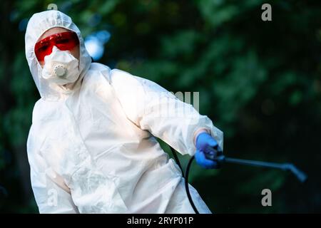 Un operaio spruzza pesticidi in un parco all'aperto. Disinfestazione. Foto Stock