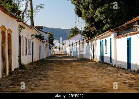 Tipica strada acciottolata coperta di fango dall'alta marea, con edifici coloniali e alberi nel tardo pomeriggio al sole in histor Foto Stock